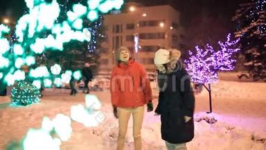 两个年轻的女孩在冬天穿过城市装饰的街道。 新年，假日，雪